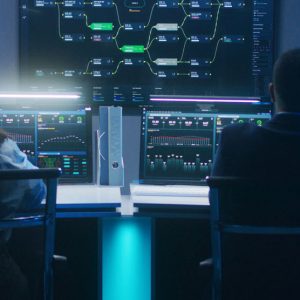 Back view of diverse IT technical specialists working on computers with database server in modern monitoring office at night. Big digital screens with real-time analysis charts and blockchain network.